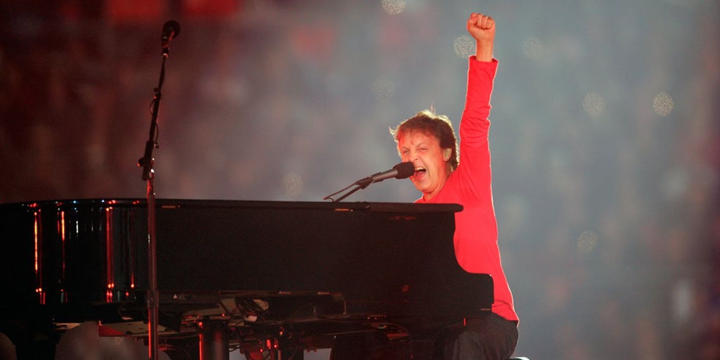 Paul McCartney wearing red sitting at a piano with his fist in the air at the 2005 Super Bowl