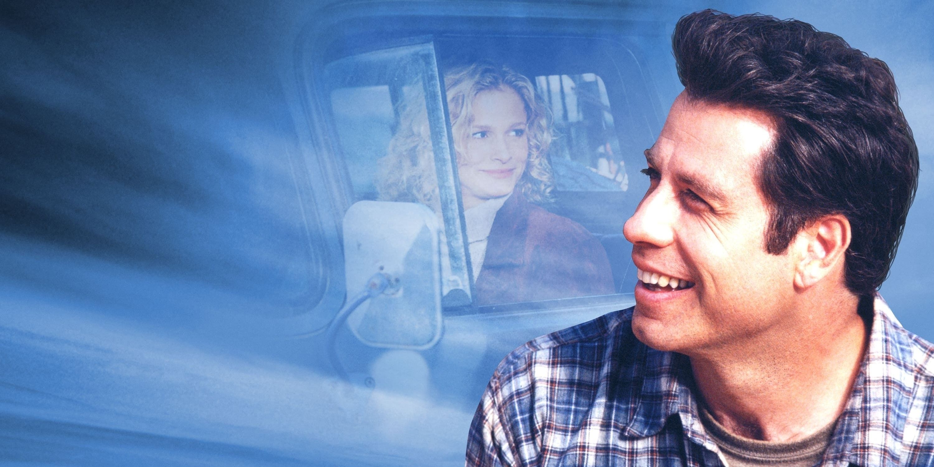 George, played by actor John Travolta, looks to the side and smiles, with Lace, played by Kyra Sedgwick, sitting in a truck in the background.