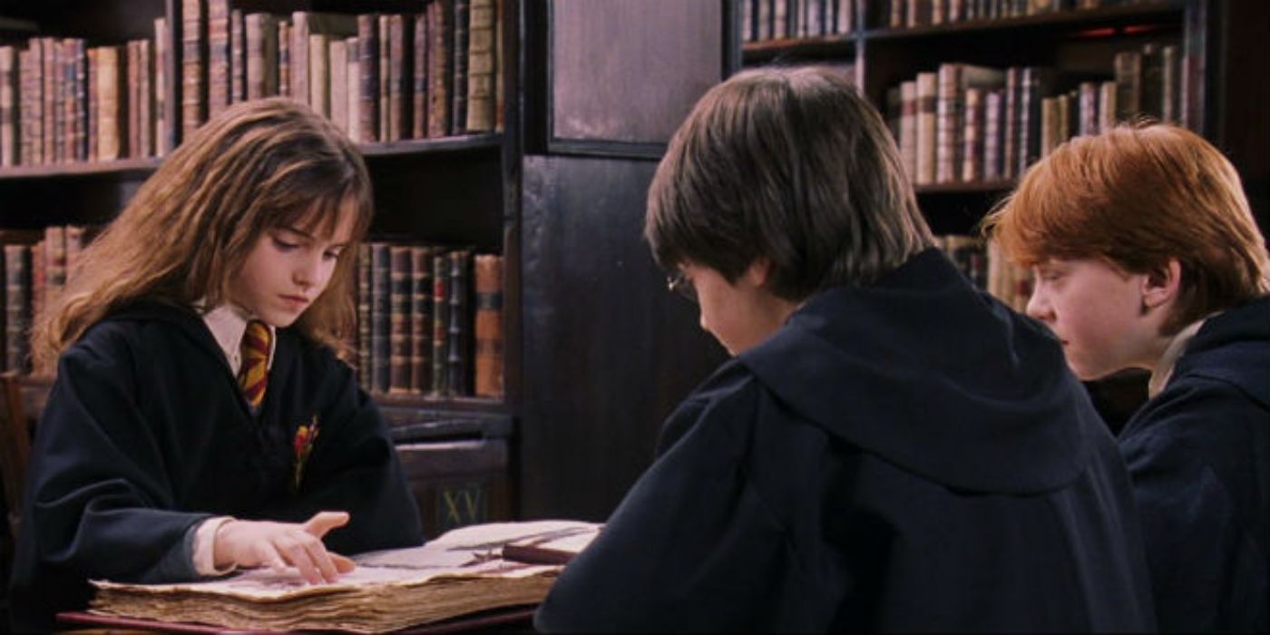 Hermione (Emma Watson), Harry (Daniel Radcliffe), and Ron (Rupert Grint) sit around the library table, reading a thick medieval-looking book.