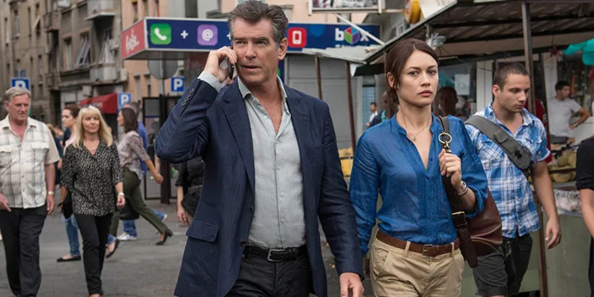 Pierce Brosnan on the phone while walking with Olga Kurylenko in a crowd of people in The November Man (2014)