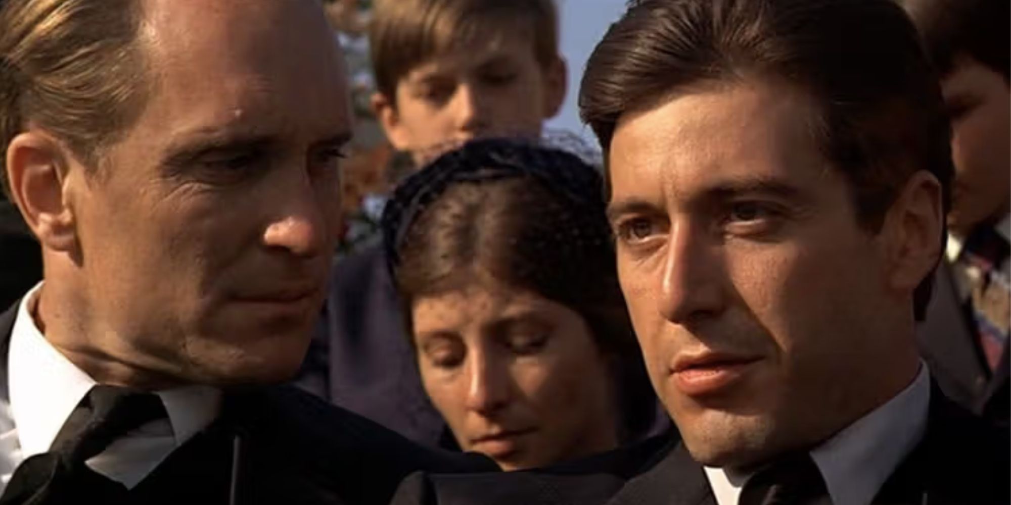 Robert Duvall sitting next to Al Pacino looking at him in The Godfather (1972)