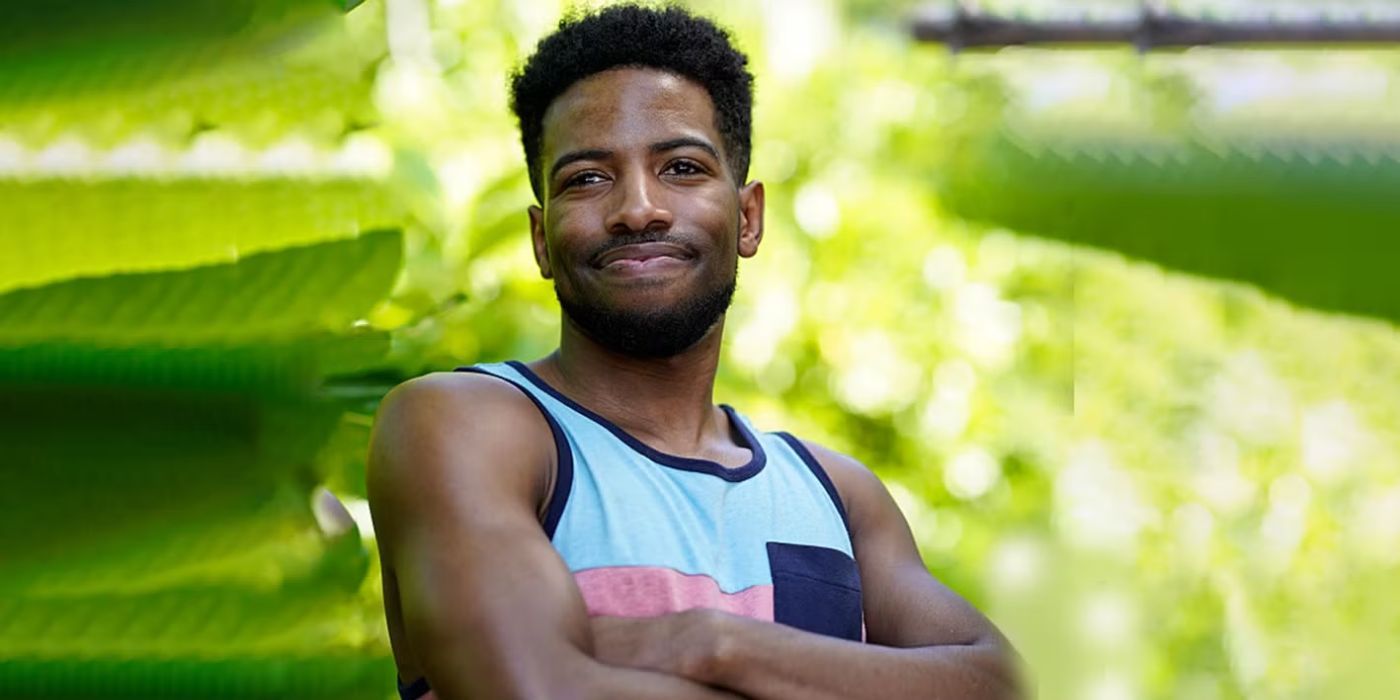 Rome Cooney stands with his arms folded with lush trees behind him on Survivor, Season 47.