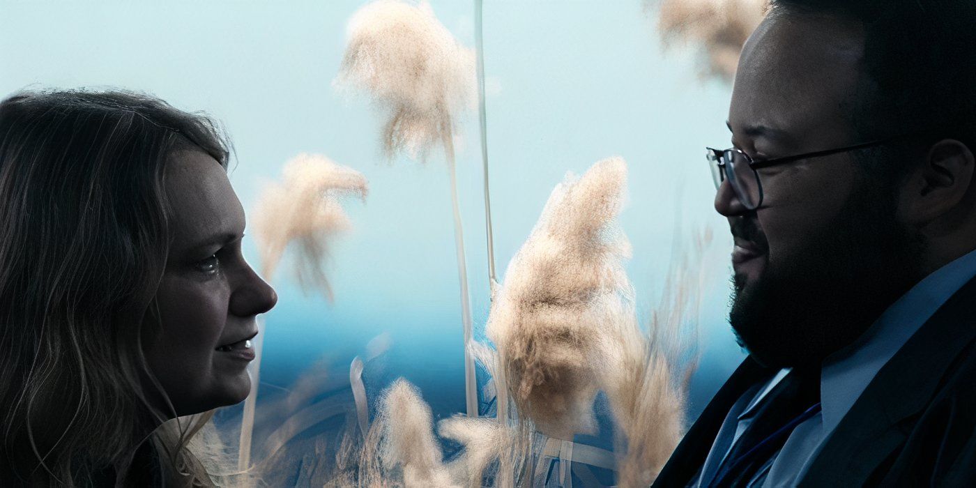 Gretchen (Merritt Wever) looks lovingly at her husband&rsquo;s innie (Zach Cherry) during an Outie Family Visitation session surrounded by a fake wheat field in Severance on Apple TV+.