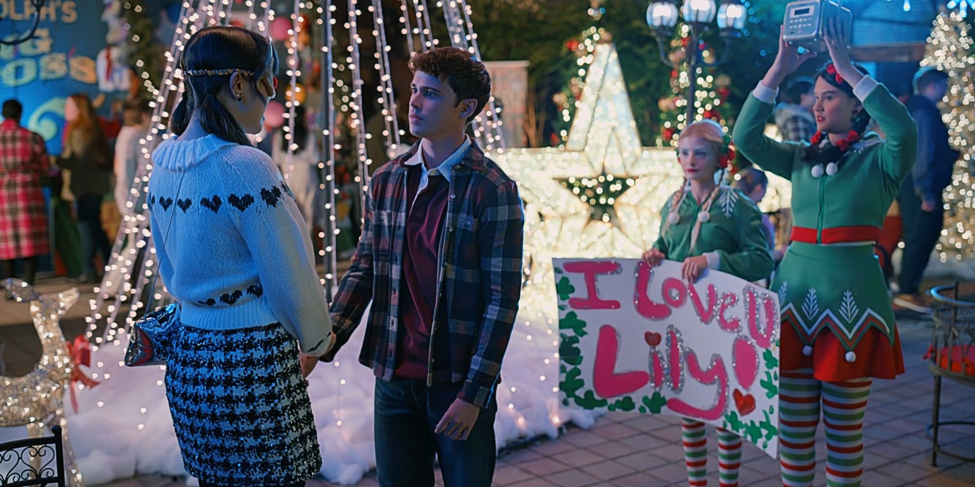 Lily and Kyle sharing a moment at the Christmas festival as Willow holds up an "I Love U Lily!" sign and Sophie holds up a radio in Sweet Magnolias Season 4