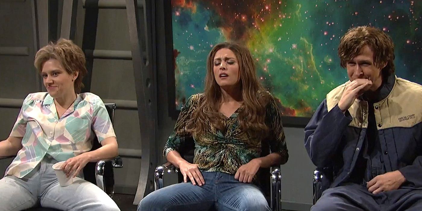 Kate McKinnon, Cecily Strong, and Ryan Gosling sitting in chairs, Gosling trying to hide a laugh on SNL.