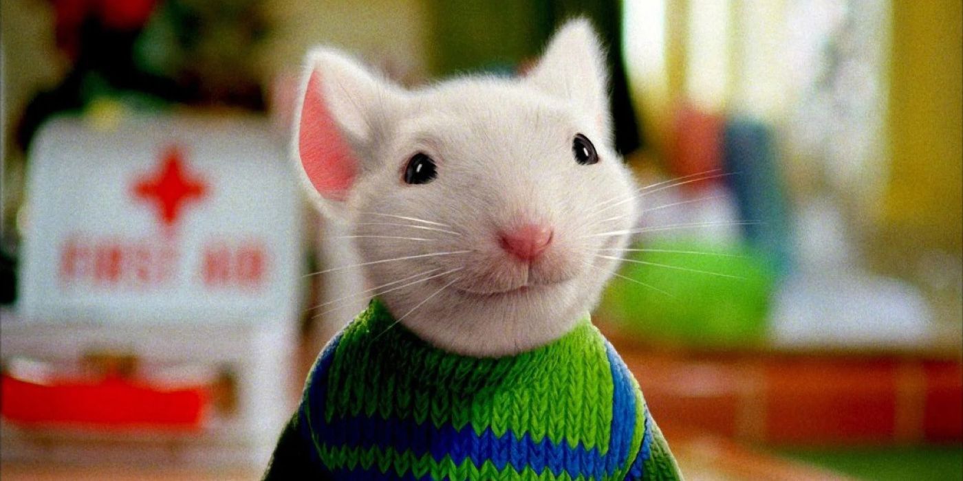 The tiny, white mouse Stuart smiles sweetly, wearing a green and blue knitted sweater in Stuart Little.