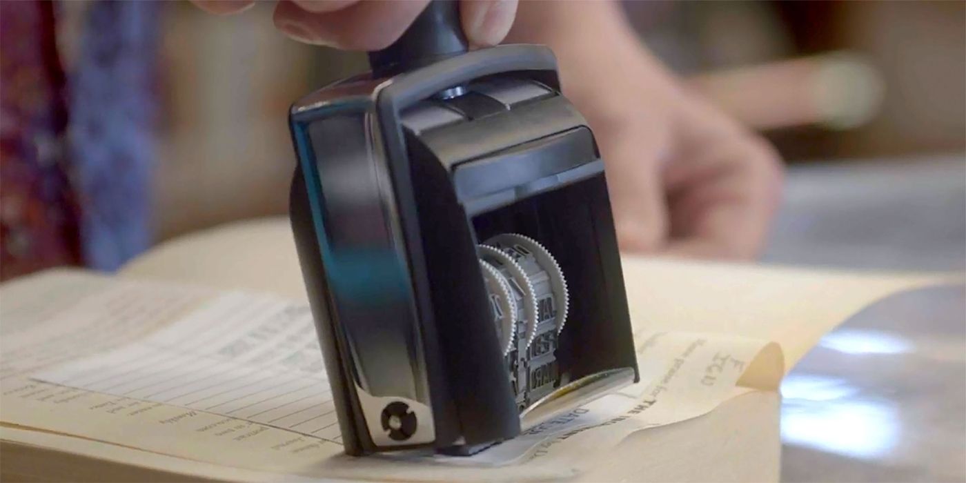 A librarian&rsquo;s hand stamping a due date on the inside of a book in The Librarians