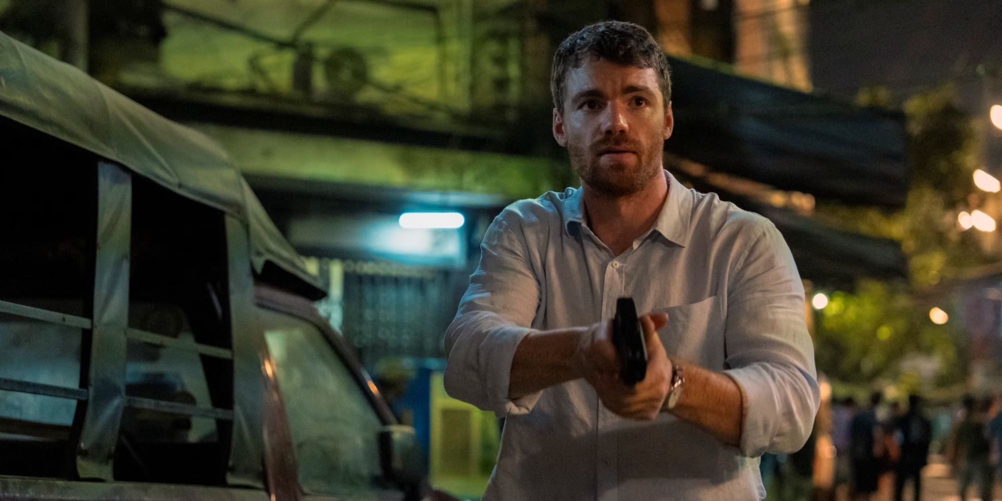 Gabriel Basso as Peter Sutherland holding a gun in Season 2 of The Night Agent.