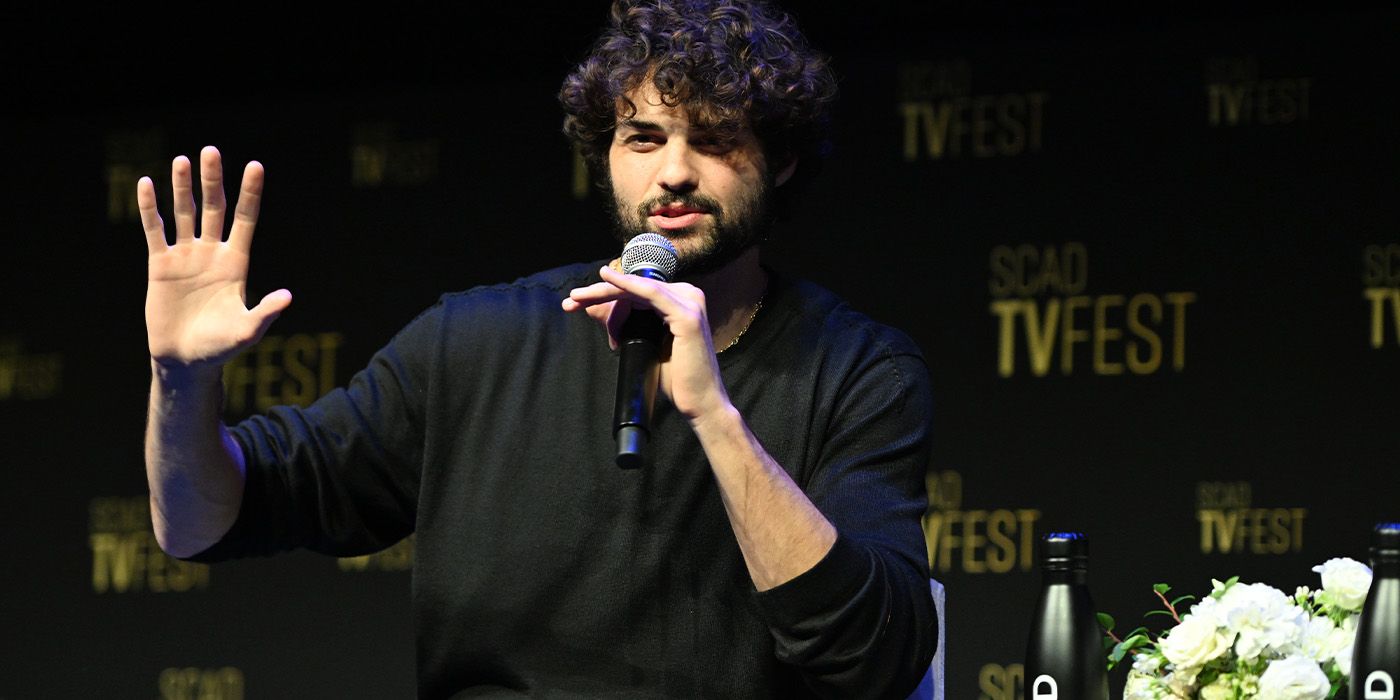 Noah Centineo speaking into a microphone on the stage of 2025 SCAD TVFest for The Recruit