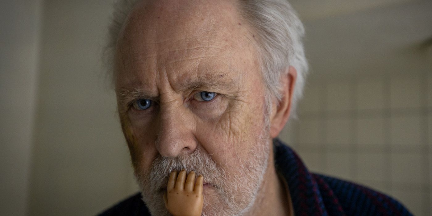 John Lithgow with a babydoll hand covering his mouth in The Rule of Jenny Pen