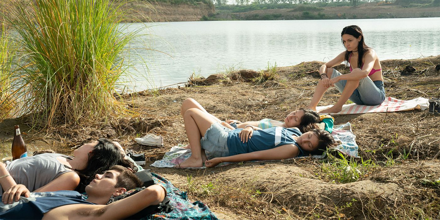 Dolores Oliverio sitting in front of a group of young people lying at the bank of a lake in The Virgin of Quarry Lake