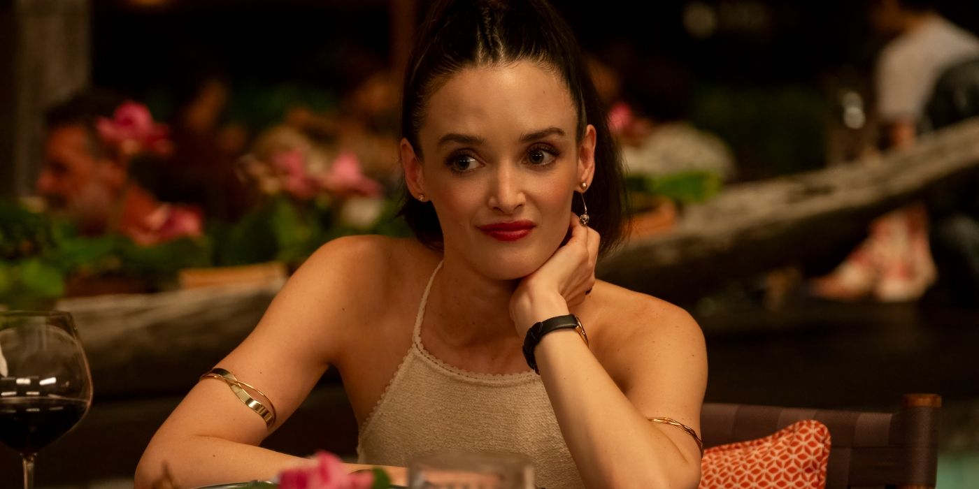 Charlotte Le Bon as Chloe sitting at table with chin resting on hand in The White Lotus Season 3, Episode 2.