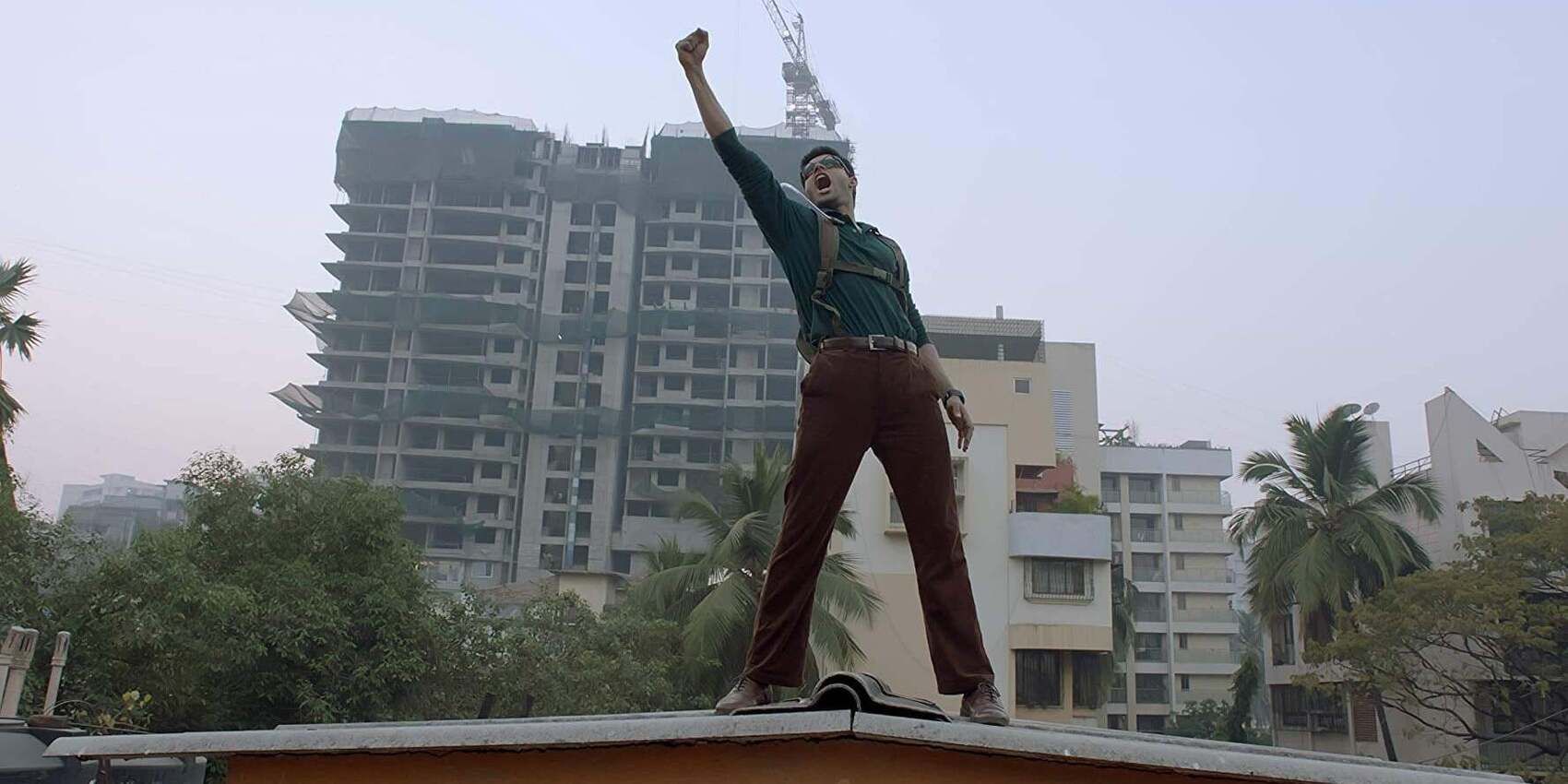 Abhimanyu Dasani as Surya standing proud on top of a building and striking a pose holding something high above his head in &lsquo;The Man Who Feels No Pain&rsquo; (2018)
