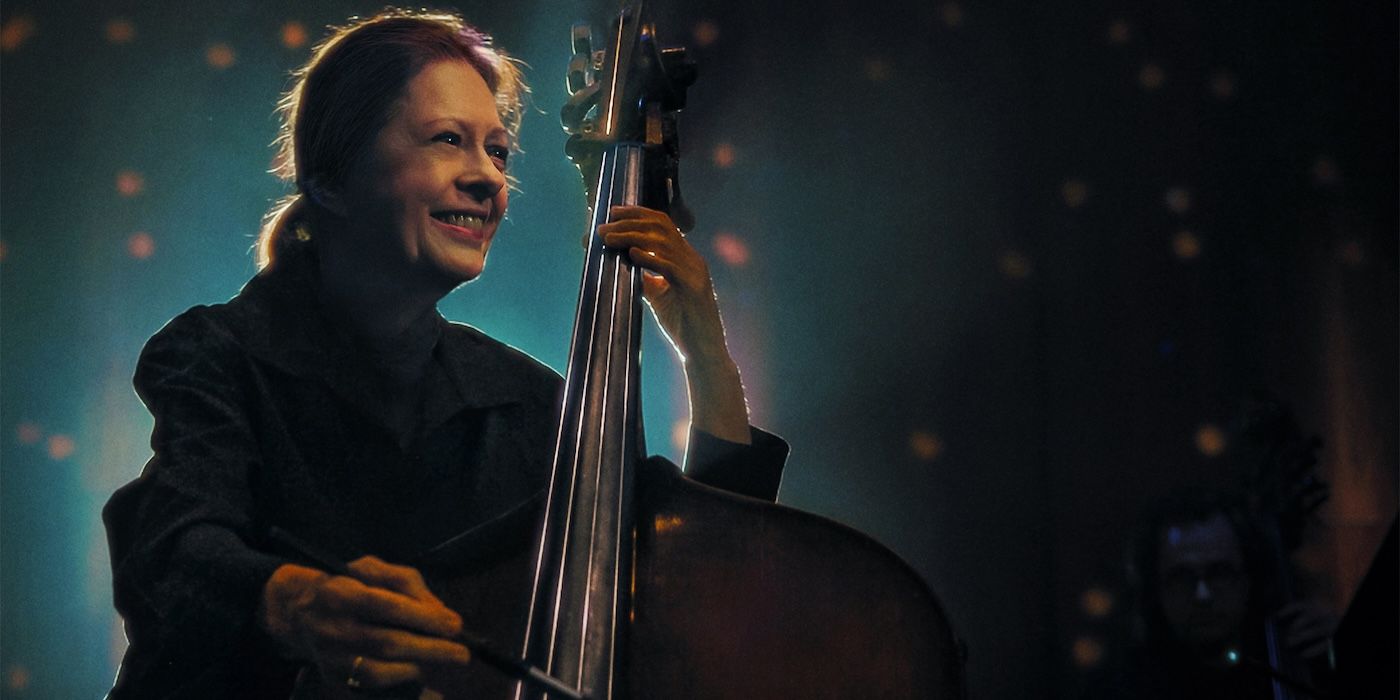 A woman smiling while playing the cello in The Only Girl in the Orchestra