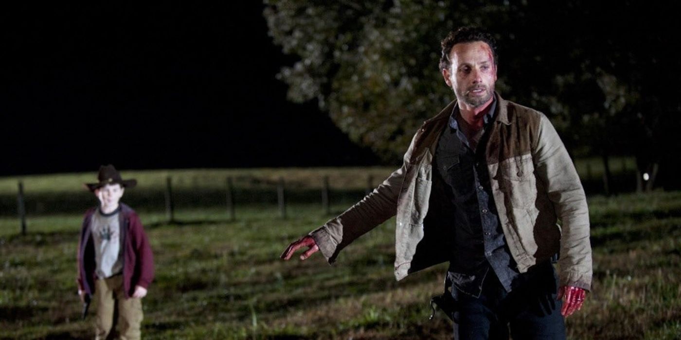 Rick with his hand out, Carl blurred in the background while in the middle of a field in The Walking Dead.