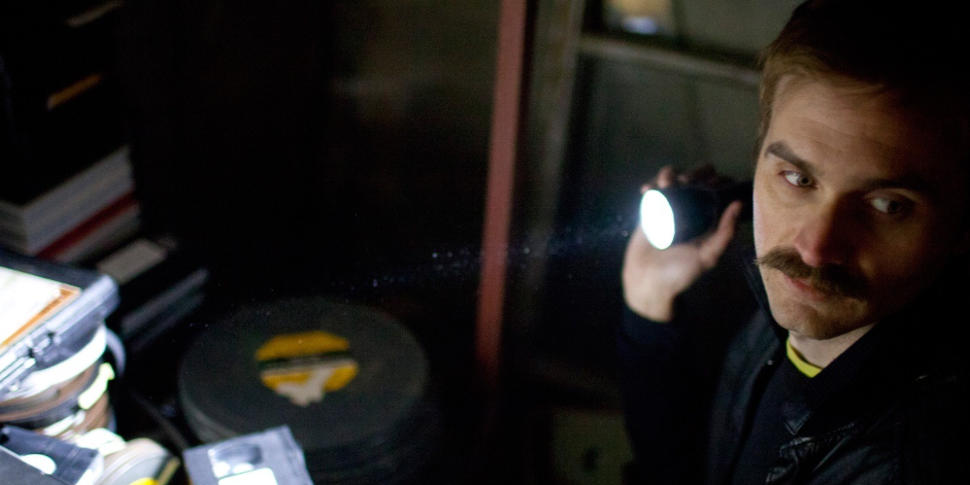 A man shines a flashlight in a dark room in V/H/S (2012)