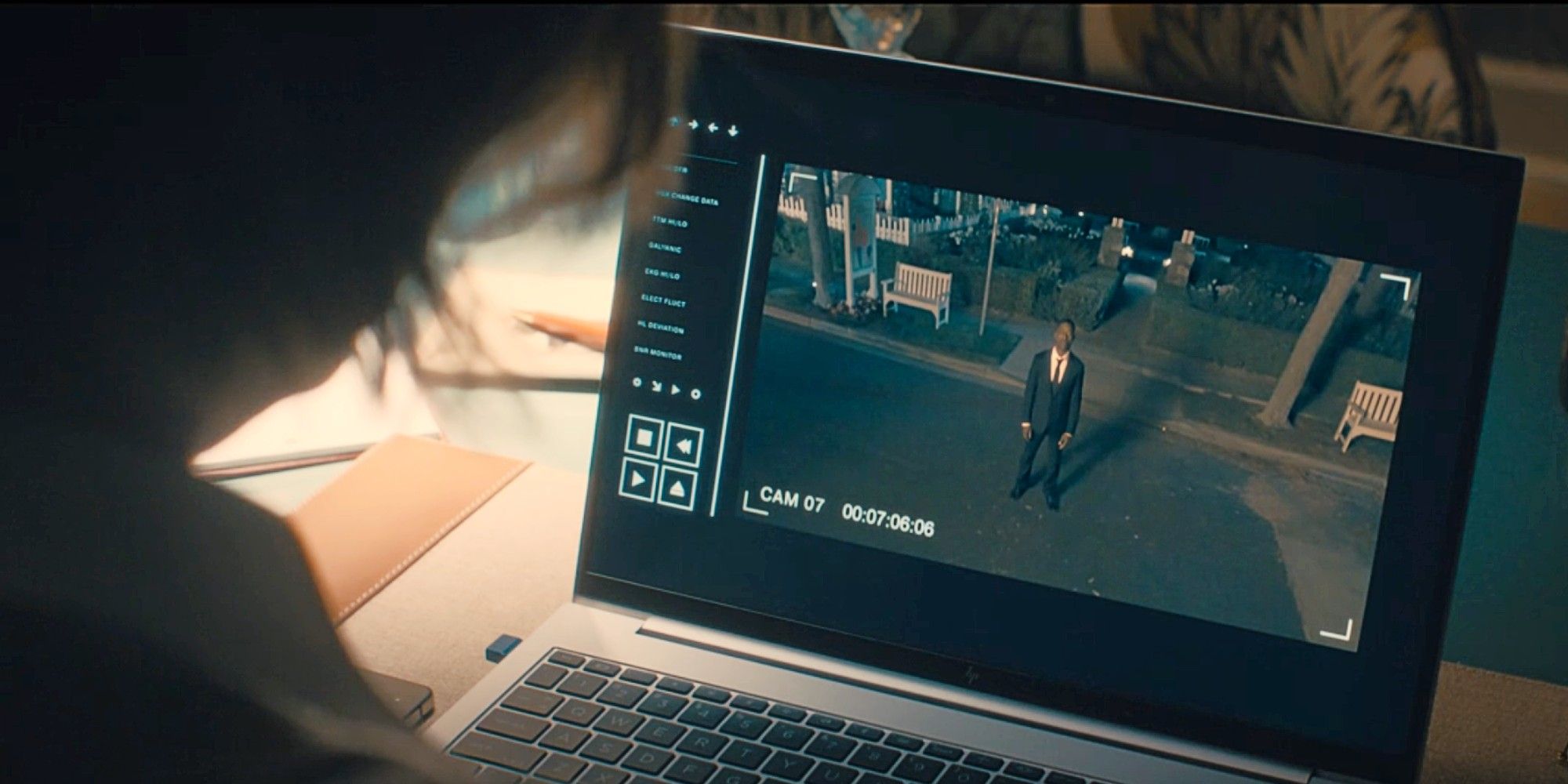 Sinatra looking at her laptop screen, where Xavier stands and stares straight up at the camera, in Paradise