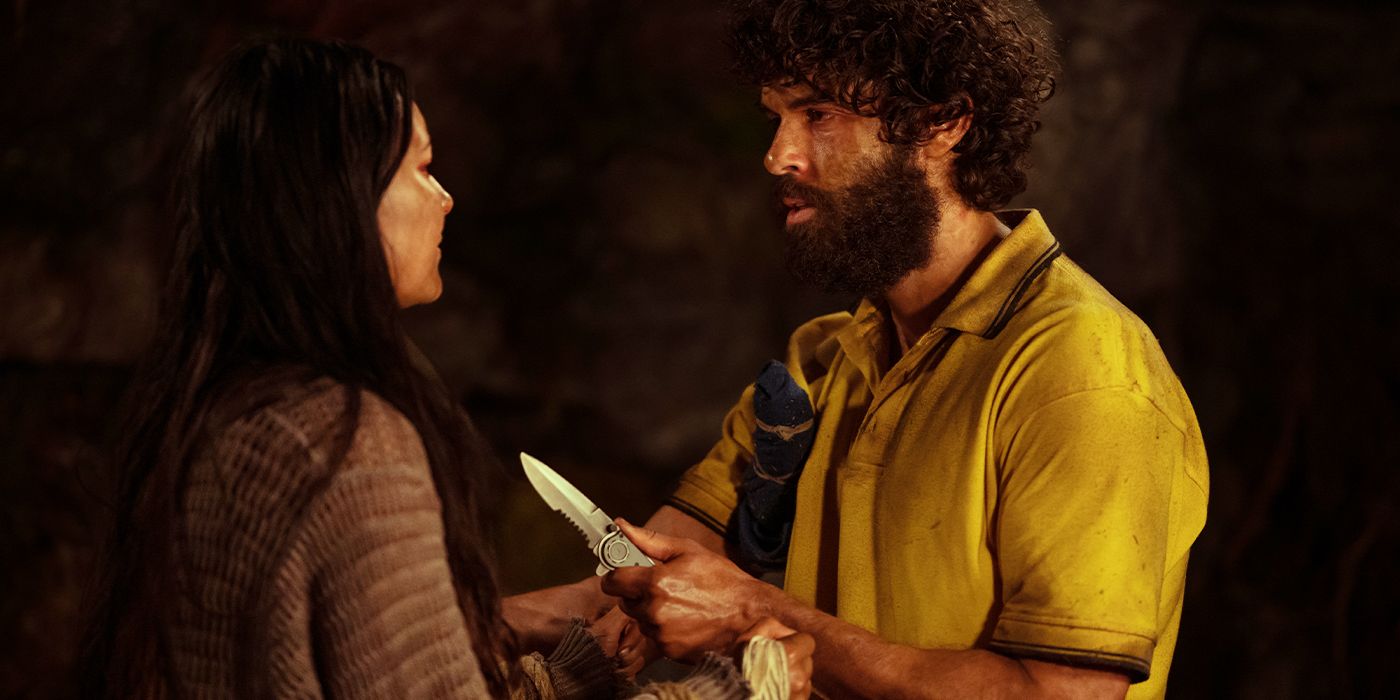 Coach Ben holding up a knife towards Mari in a cave
