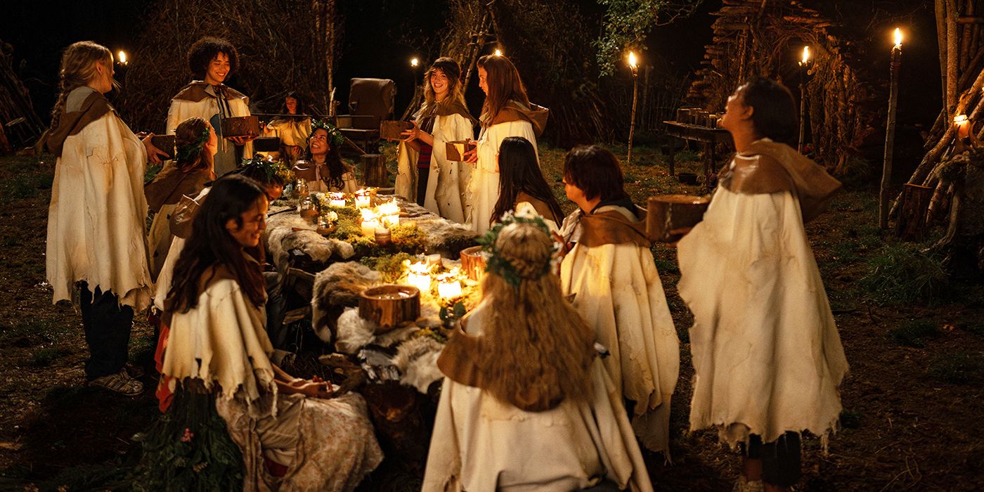 The cast of Yellowjackets Season 3 around a table in white robes and flower crowns