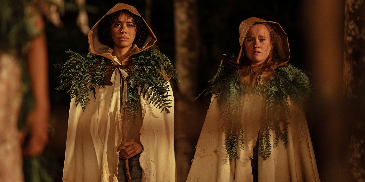 Tai and Van in ritual garb standing side by side in the woods looking concerned
