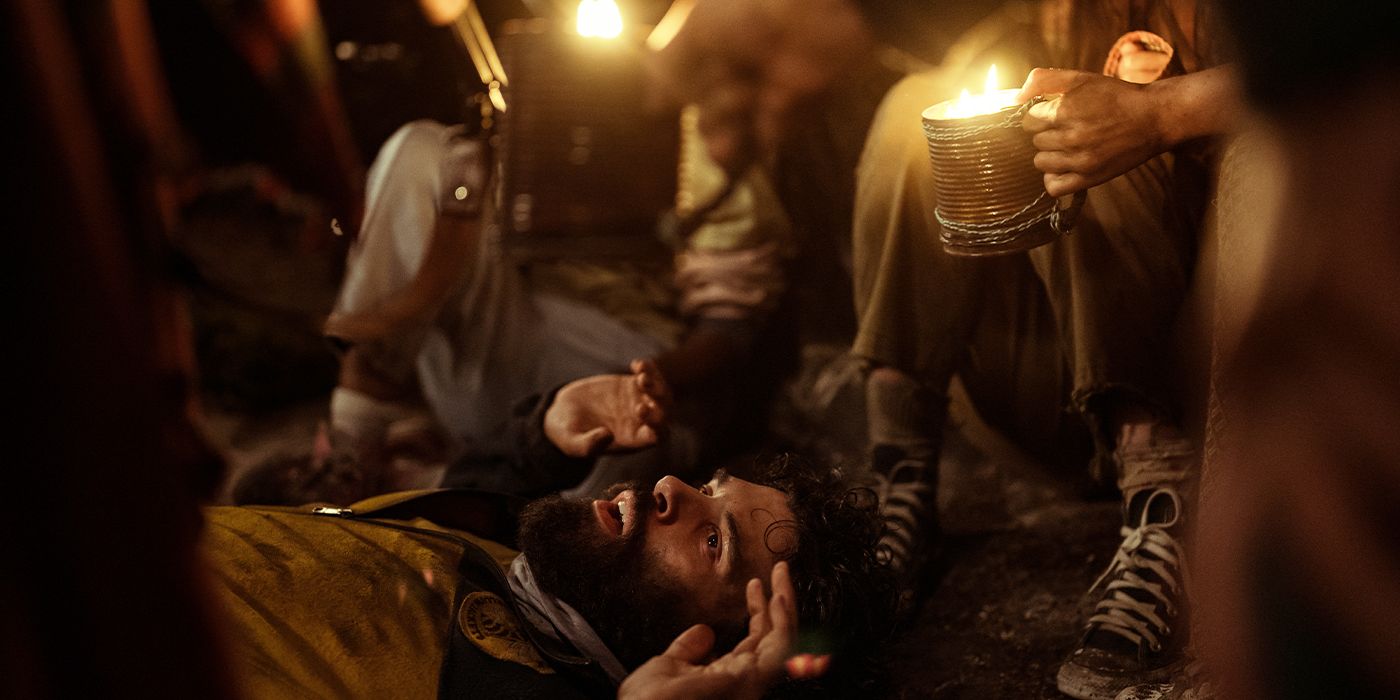 Coach Ben lying on the ground in fear surrounded by people holding candles toward him