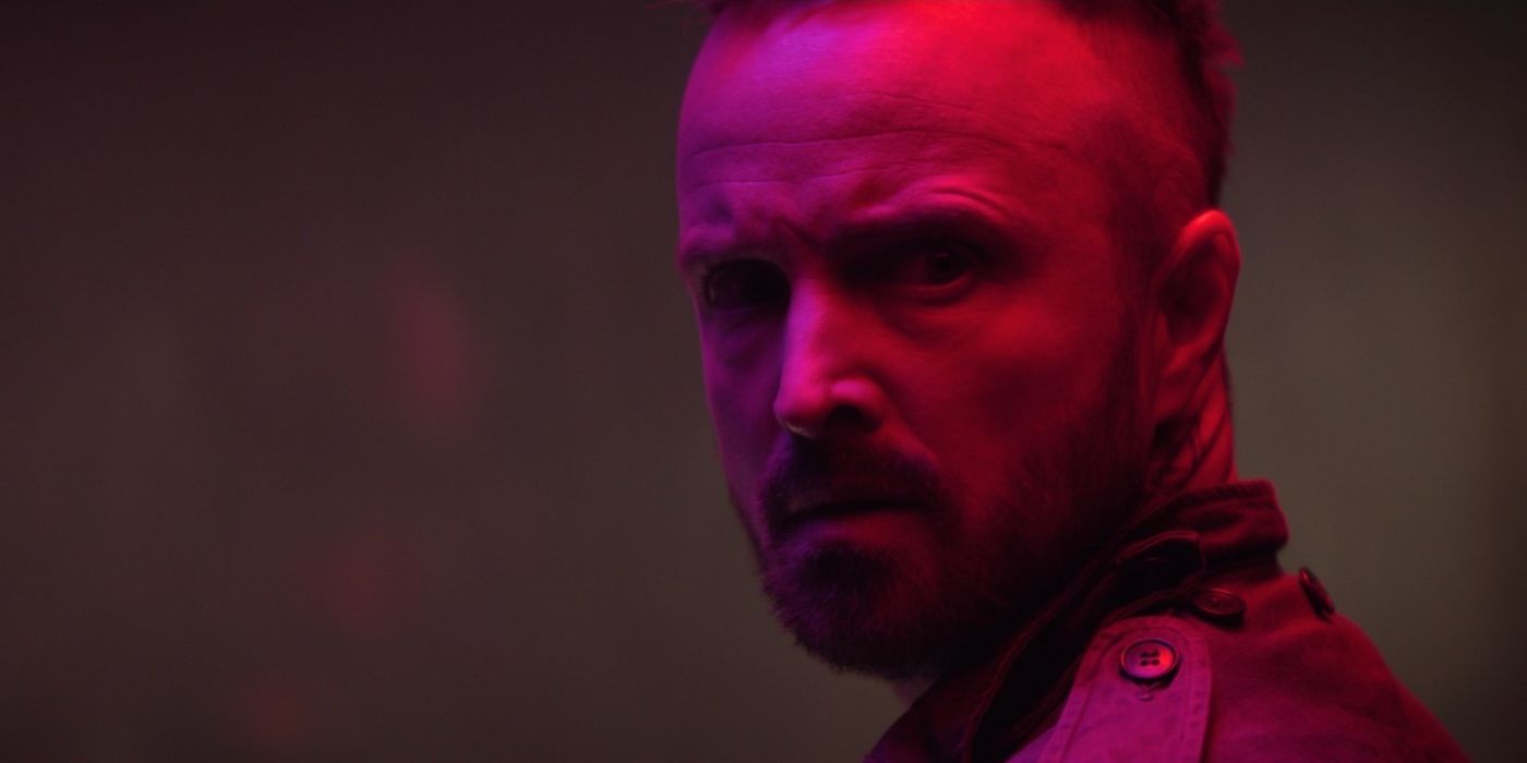 Aaron Paul as Brion, with neon-red lighting reflecting on his face in Ash.