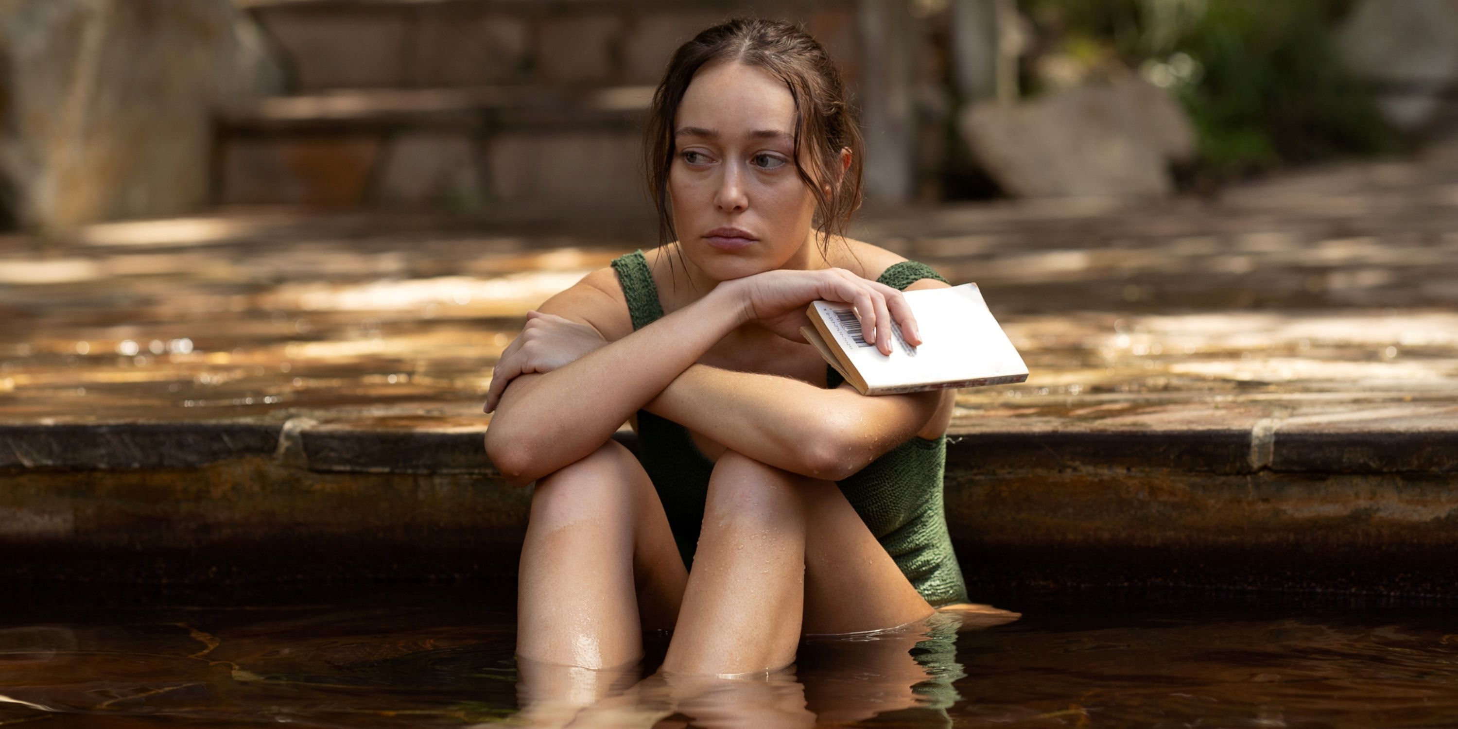 Alycia Debnam-Carey sitting in a pool in a green bathing suit in Apple Cider Vinegar