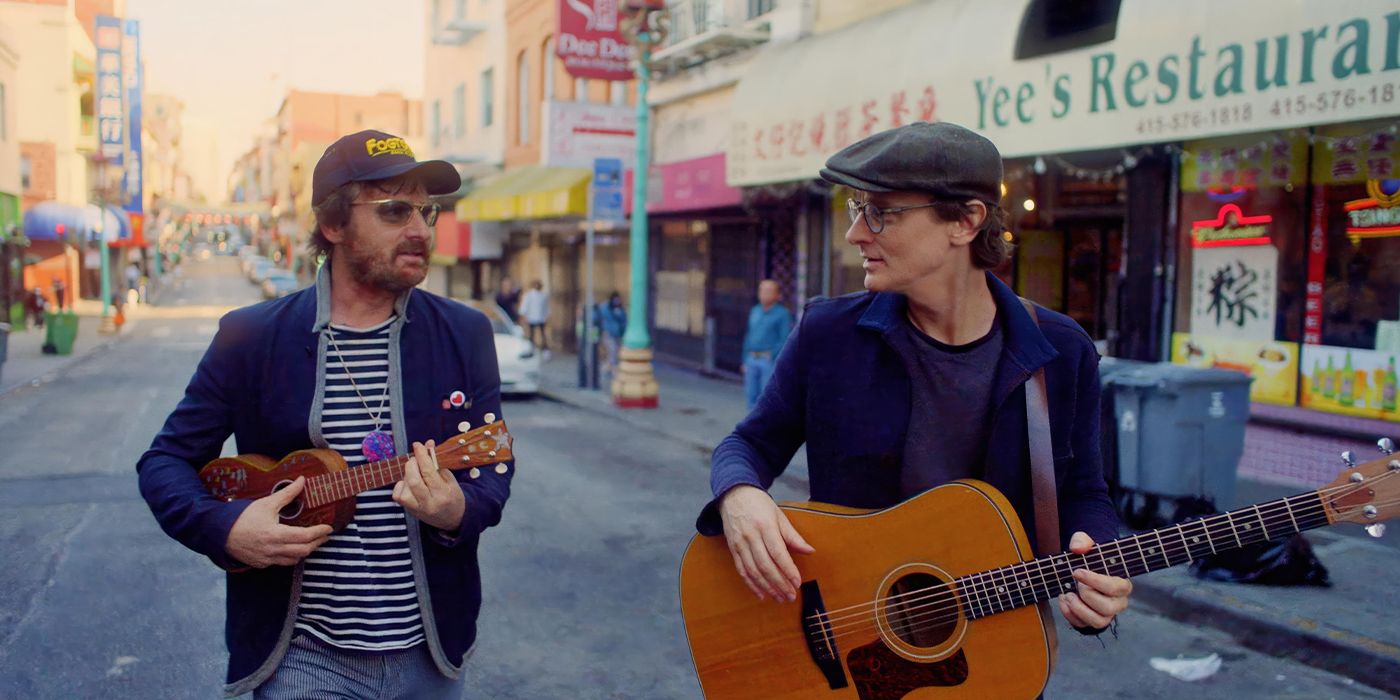 Brian Bell and Ari Gold walking down a street with instruments in Brother Verses Brother