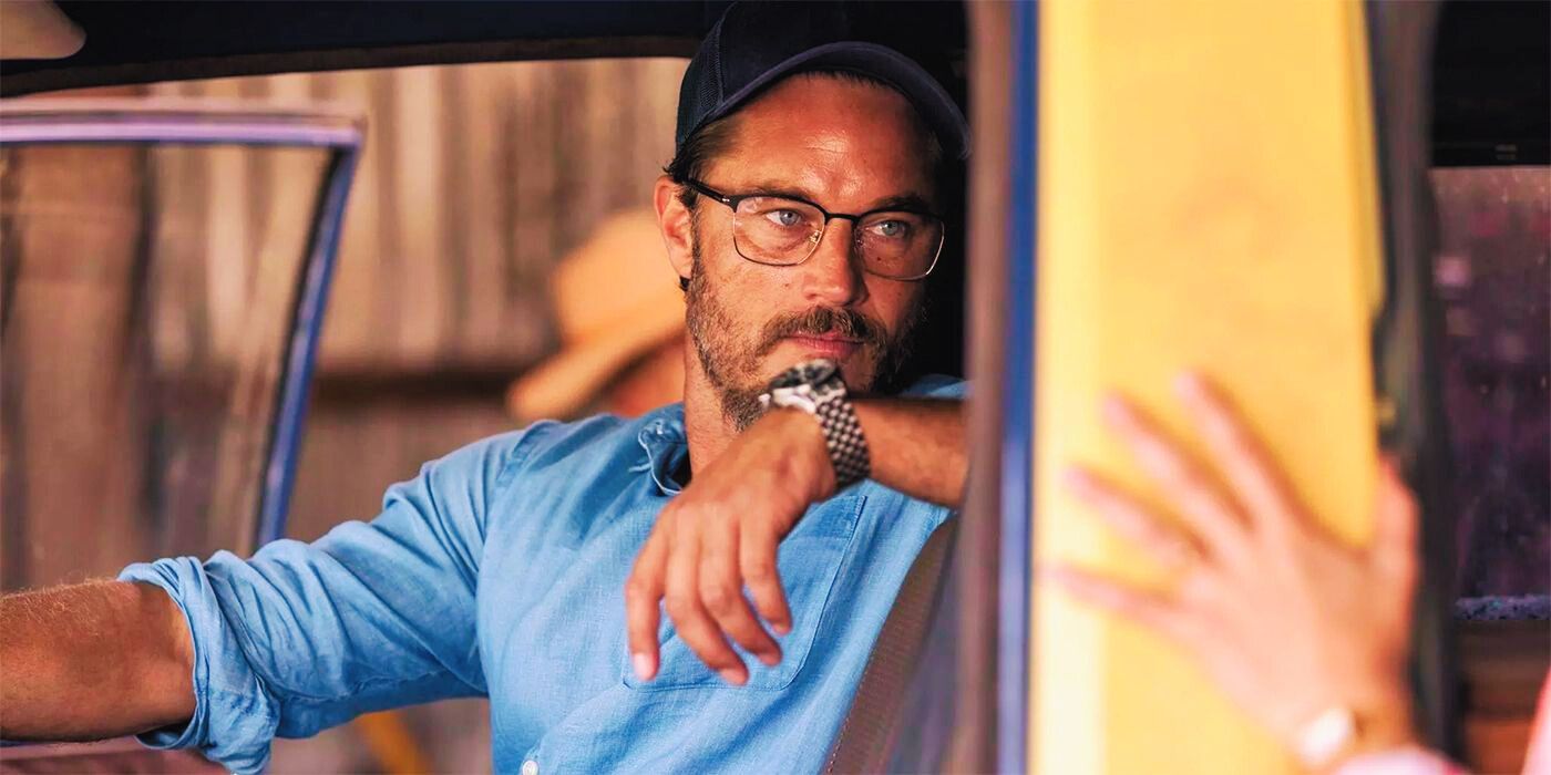 Travis Fimmel with his arm over the back of a truck seat, wearing glasses, and looking at someone