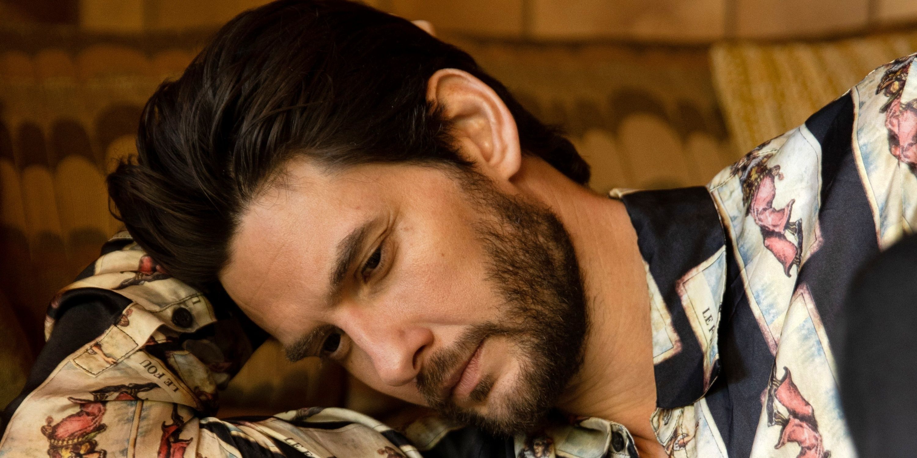 Ben Barnes in close-up leaning his right cheek on his bent right arm in a button-down shirt