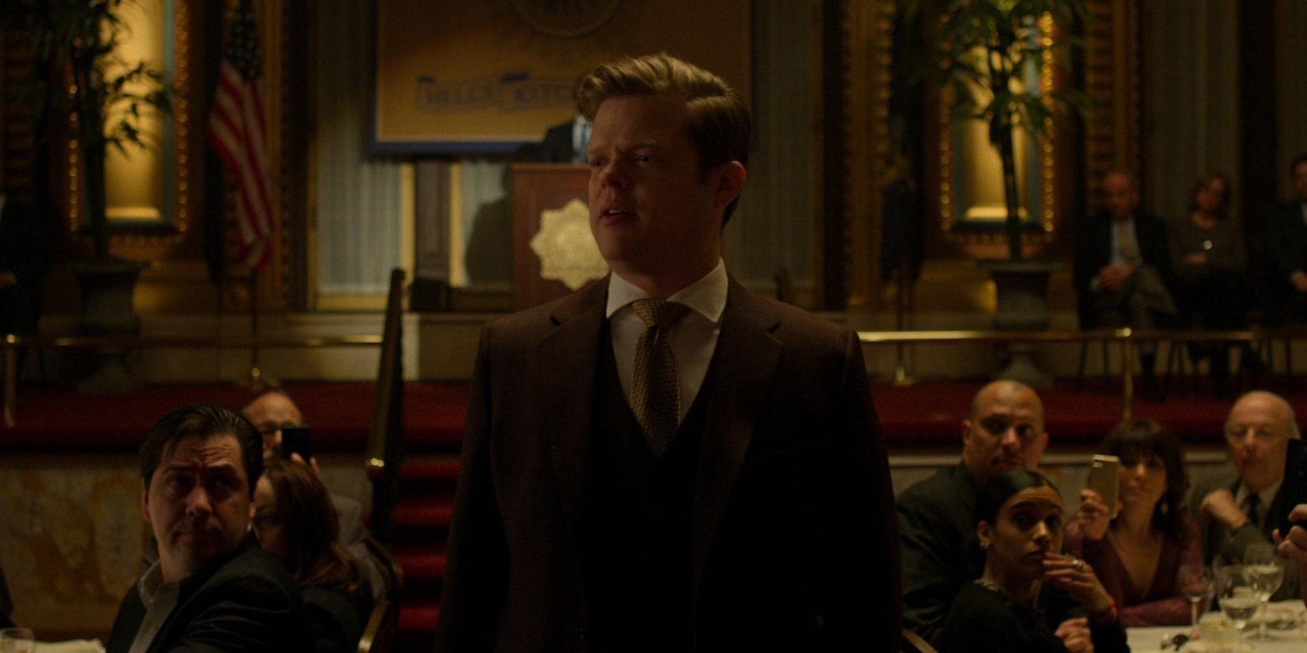 A suited man stands and addresses a crowd