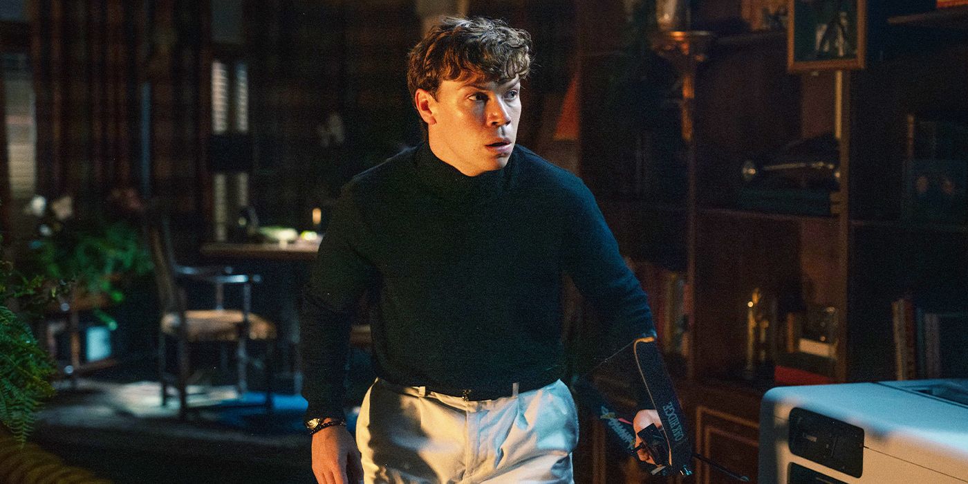 Will Poulter sneaking around a dimly lit room holding a bow looking scared in Death of a Unicorn