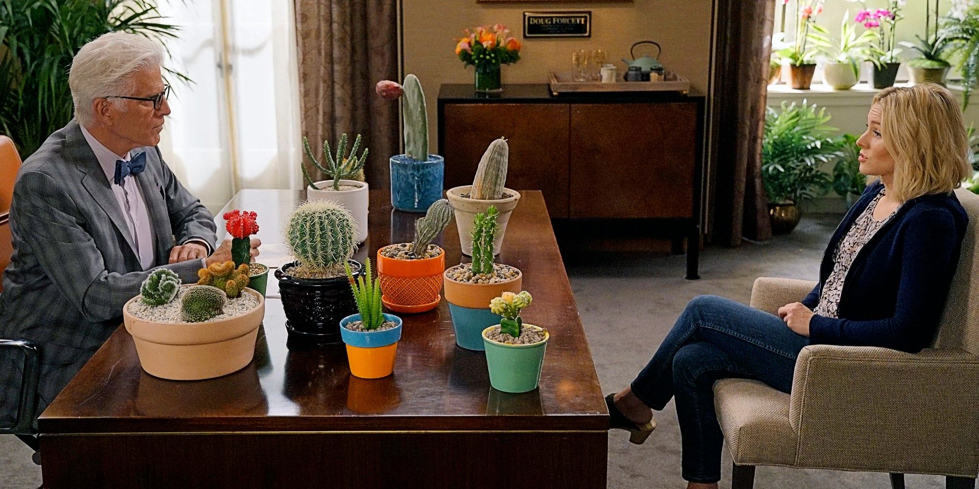 Michael sitting across from Eleanor Shellstrop, with a desk covered in cacti between them, in The Good Place Season 1 Episode 8