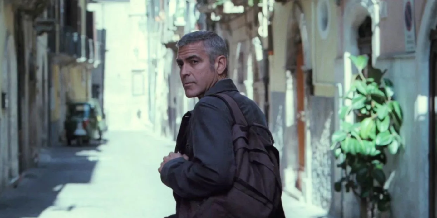 George Clooney looks back while walking in a European town in The American