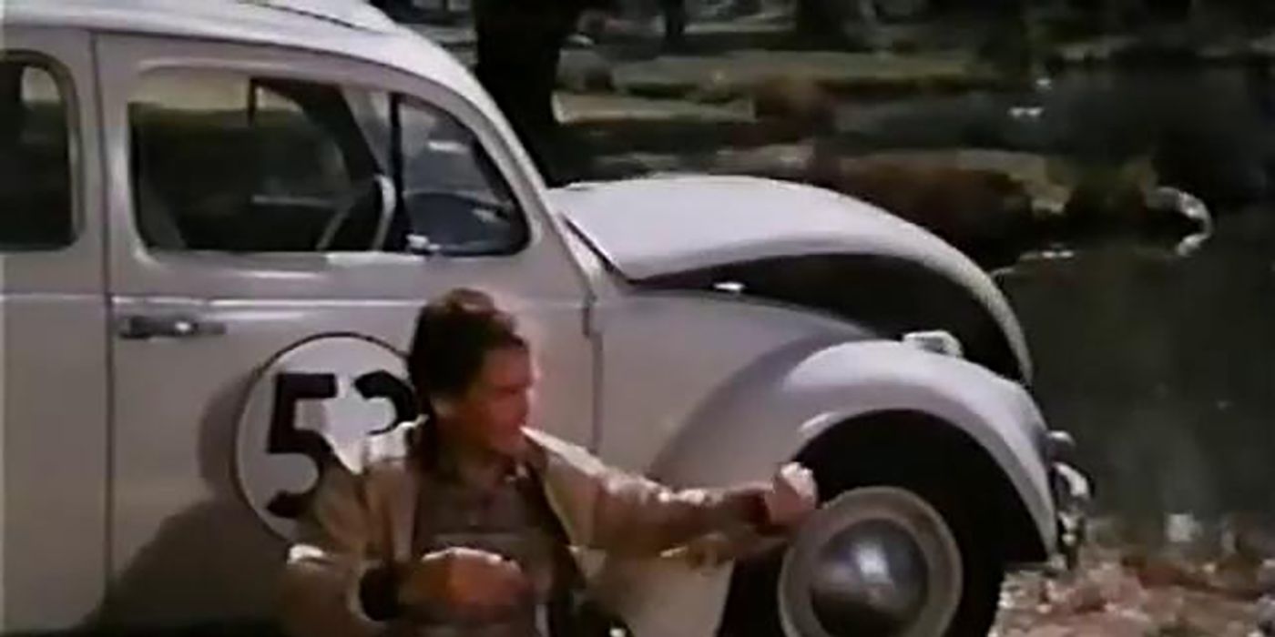 A man sits on the ground leaning against a Volkswagen Beetle in Herbie, The Love Bug