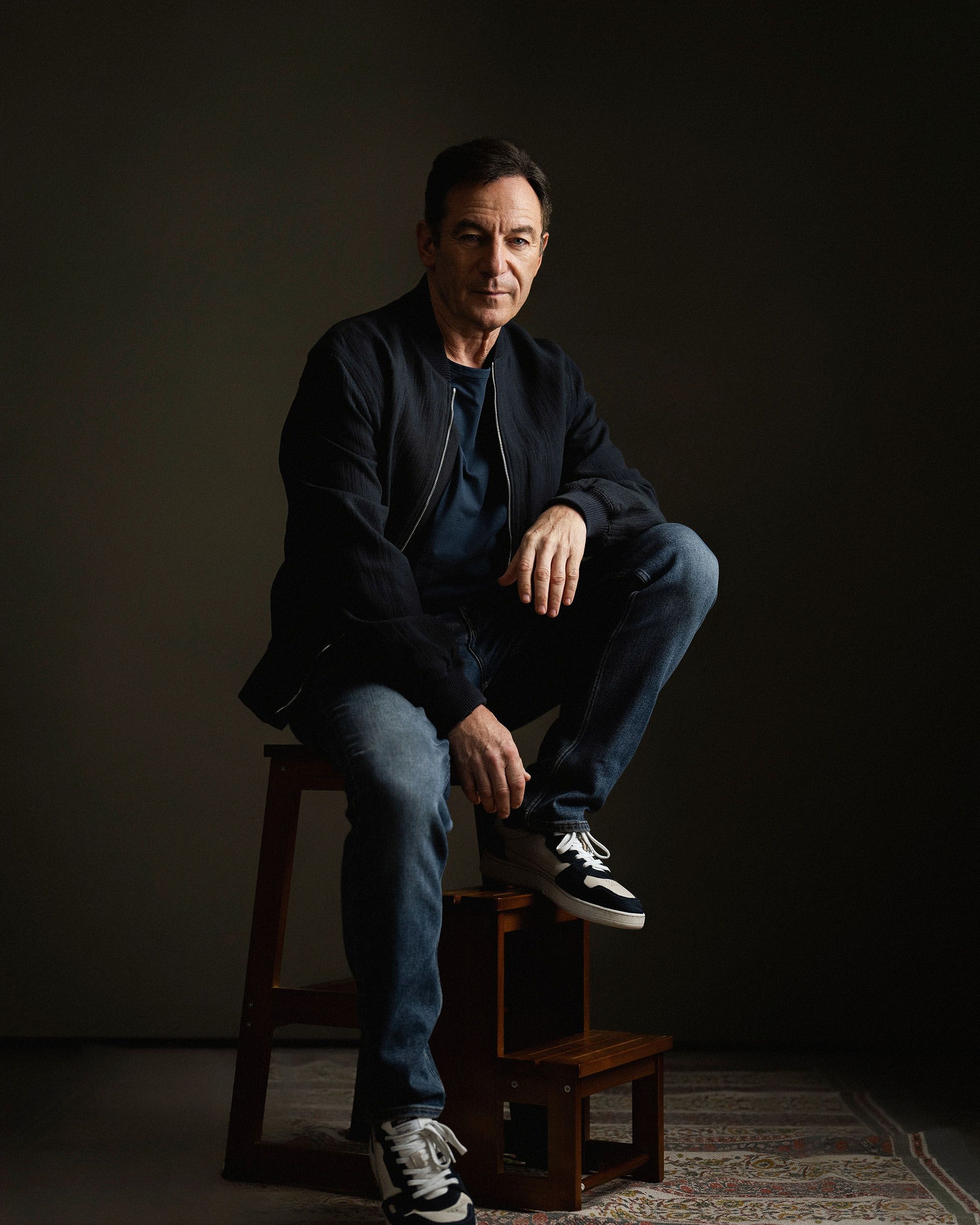 Jason Isaacs sits on a stool for a portrait session with London-based photography studio, Yellowbelly.