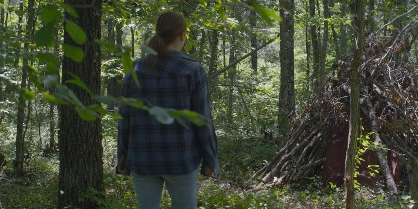 Leven Rambin standing in front of a shelter made of sticks in the middle of the woods in Lost Child.