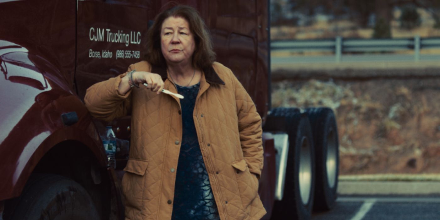 margo martindale wears a large tan jacket and leans up against the side of a red big rig