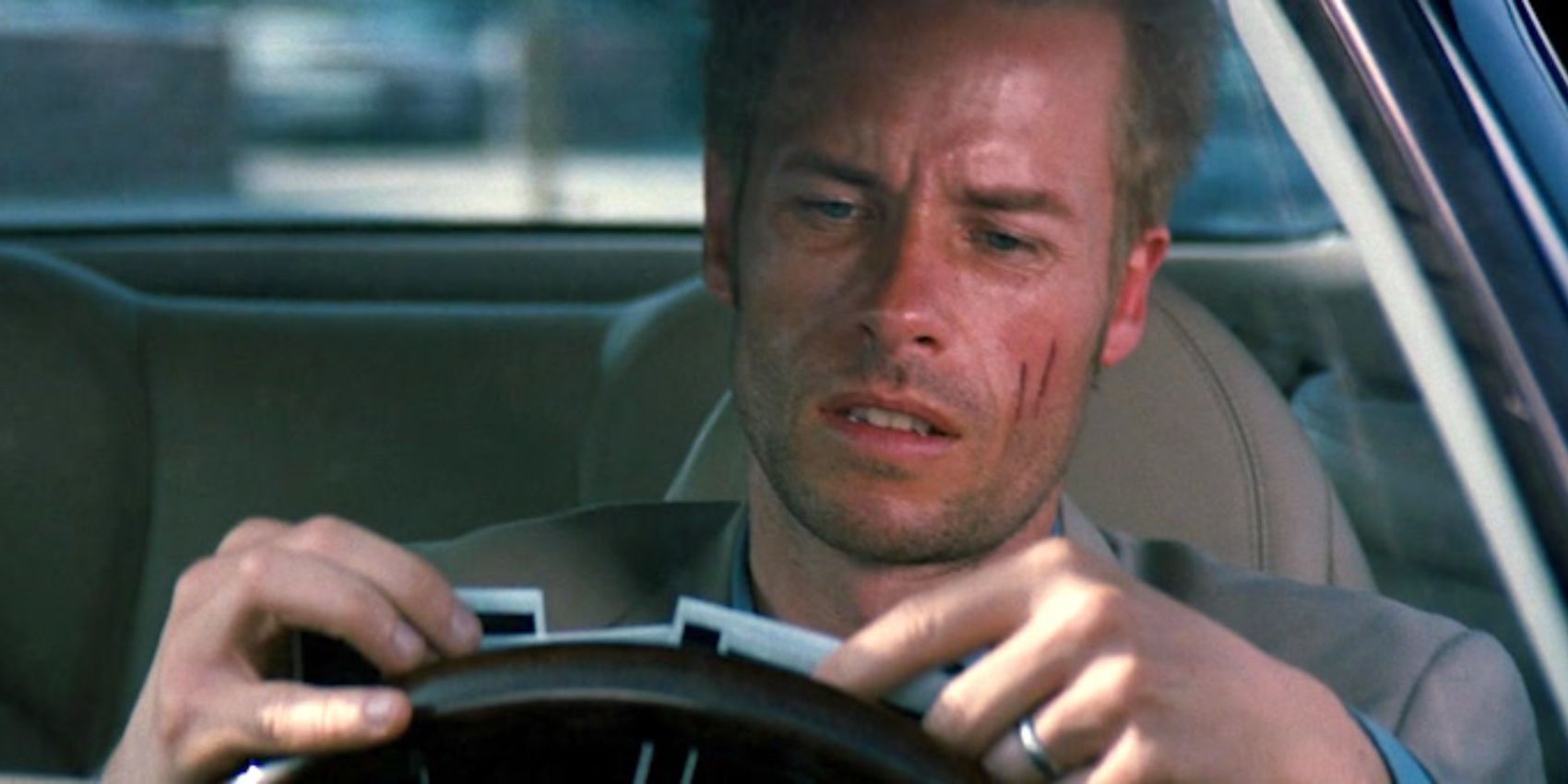 Guy Pearce looks at some polaroid photographs while sitting inside a car