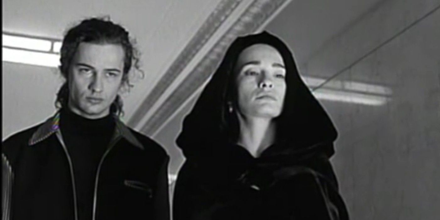 Elina Löwensohn wearing a black hooded cape while standing next to Karl Geary in a morgue hallway in Nadja.