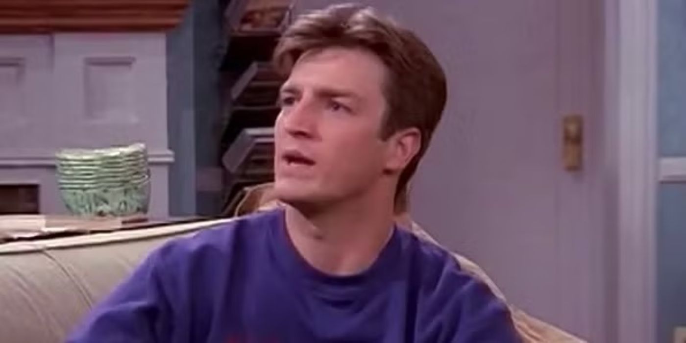 Nathan Fillion as Johnny Donnelly sitting on a couch and talking to someon off-screen in Two Guys and A Girl.