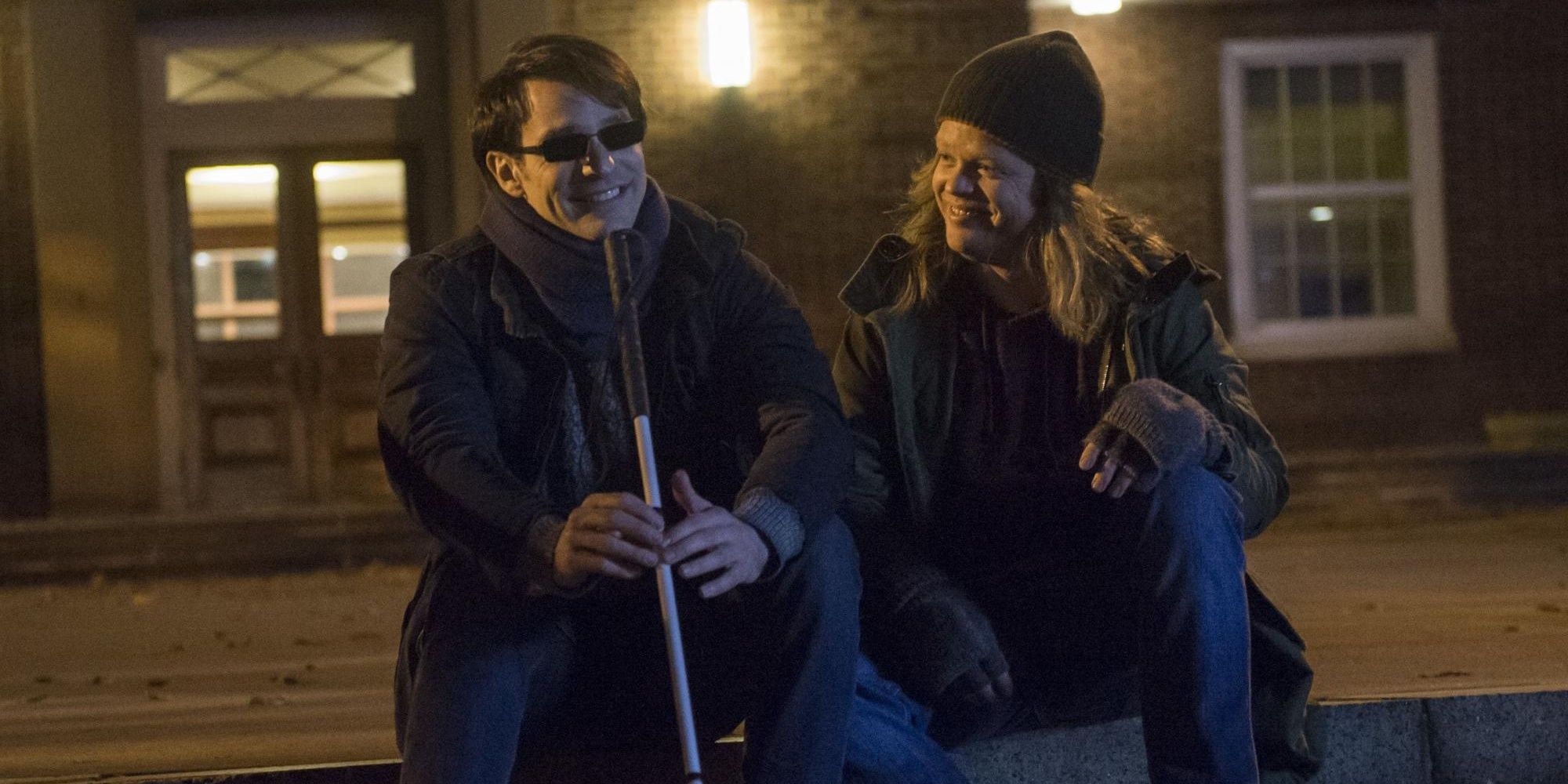 Charlie Cox as Matt Murdock and Elden Henson as Foggy sit on steps outside a building smiling in Daredevil.