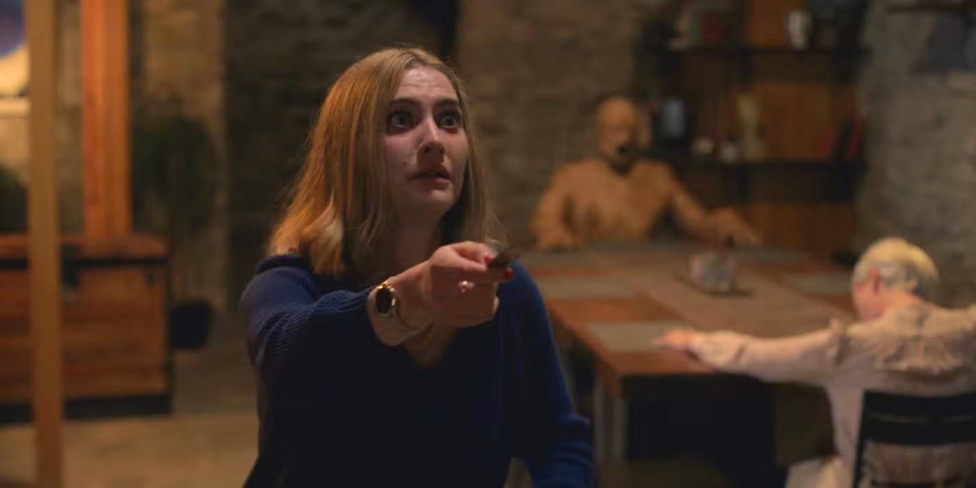 Caroline Menton holding a knife while two creepy figures sit at a table behind her in Oddity.