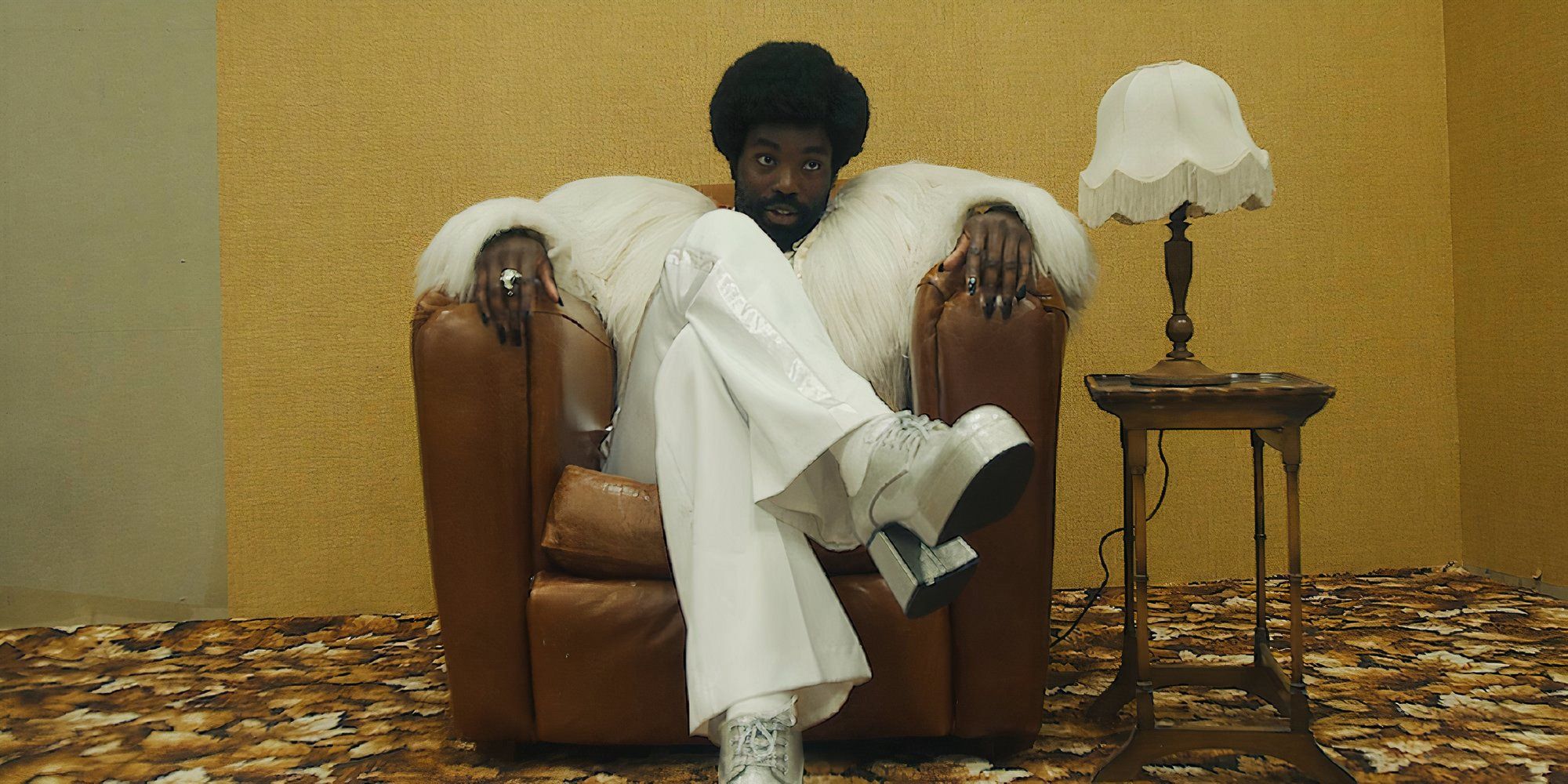 Paapa Essiedu in Black Mirror Demon 79 as Gaap sitting on a sofa chair with his legs crossed.