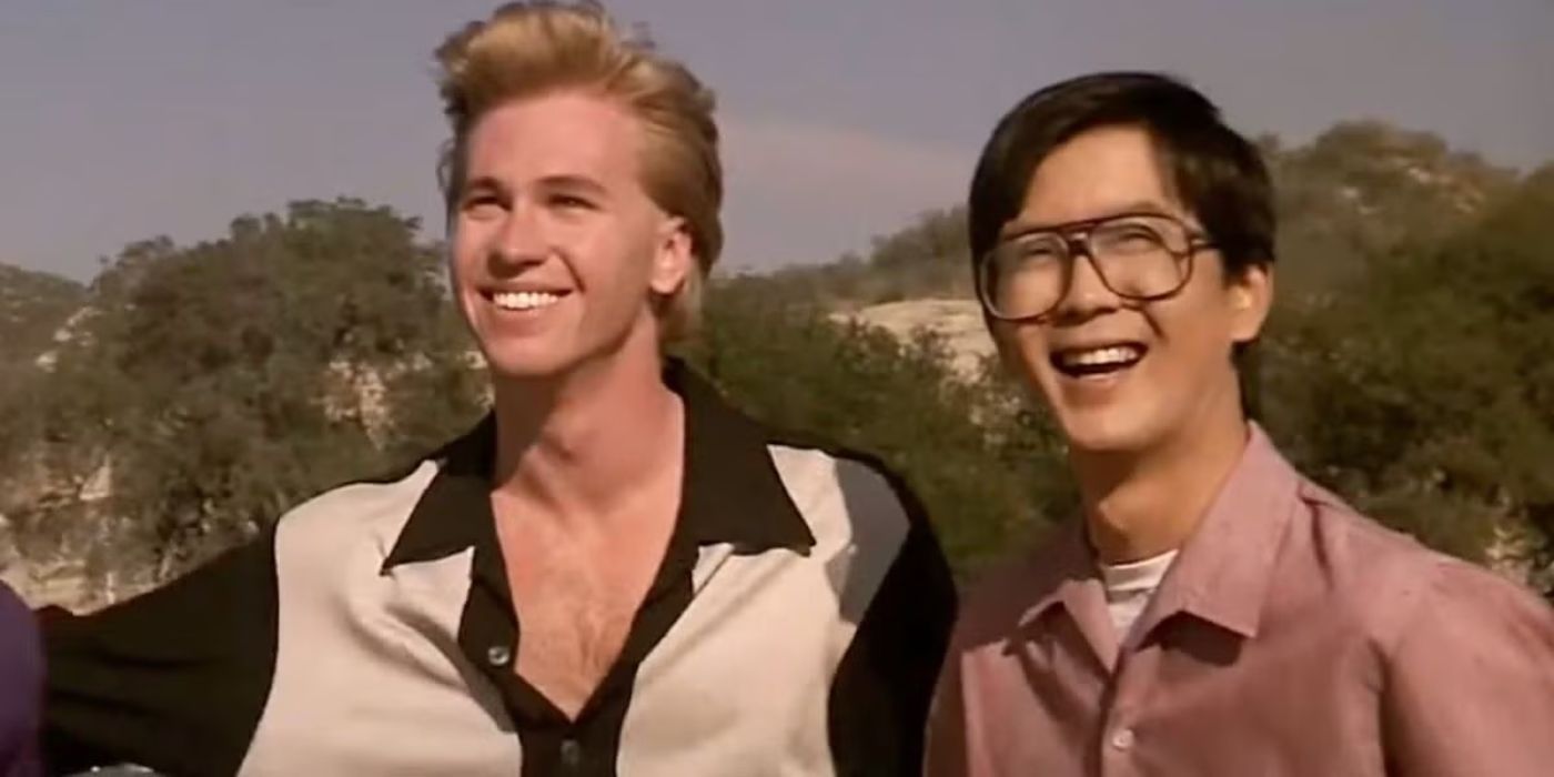 Val Kilmer and Mark Kamiyama stand outside and smile, looking happy in Real Genius.