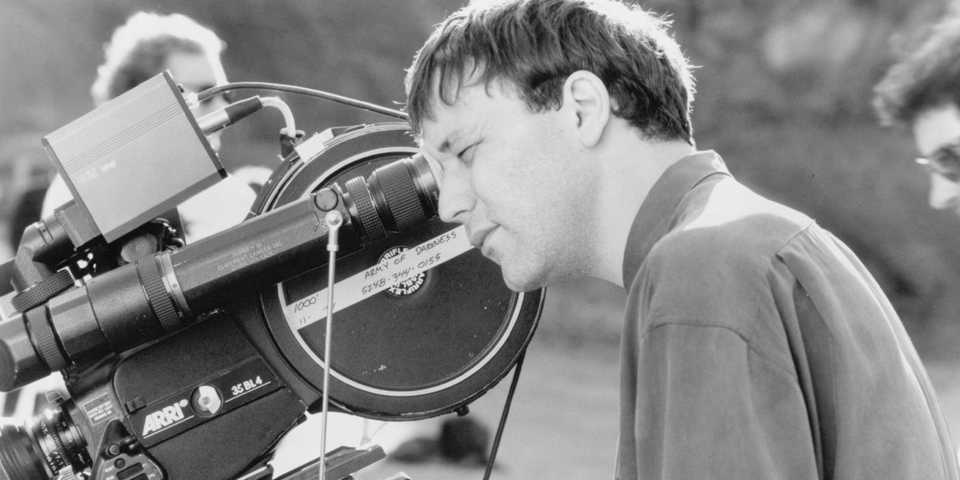 Black and white photo of Sam Raimi looking into the eyepiece of a camera on the set of Army of Darkness