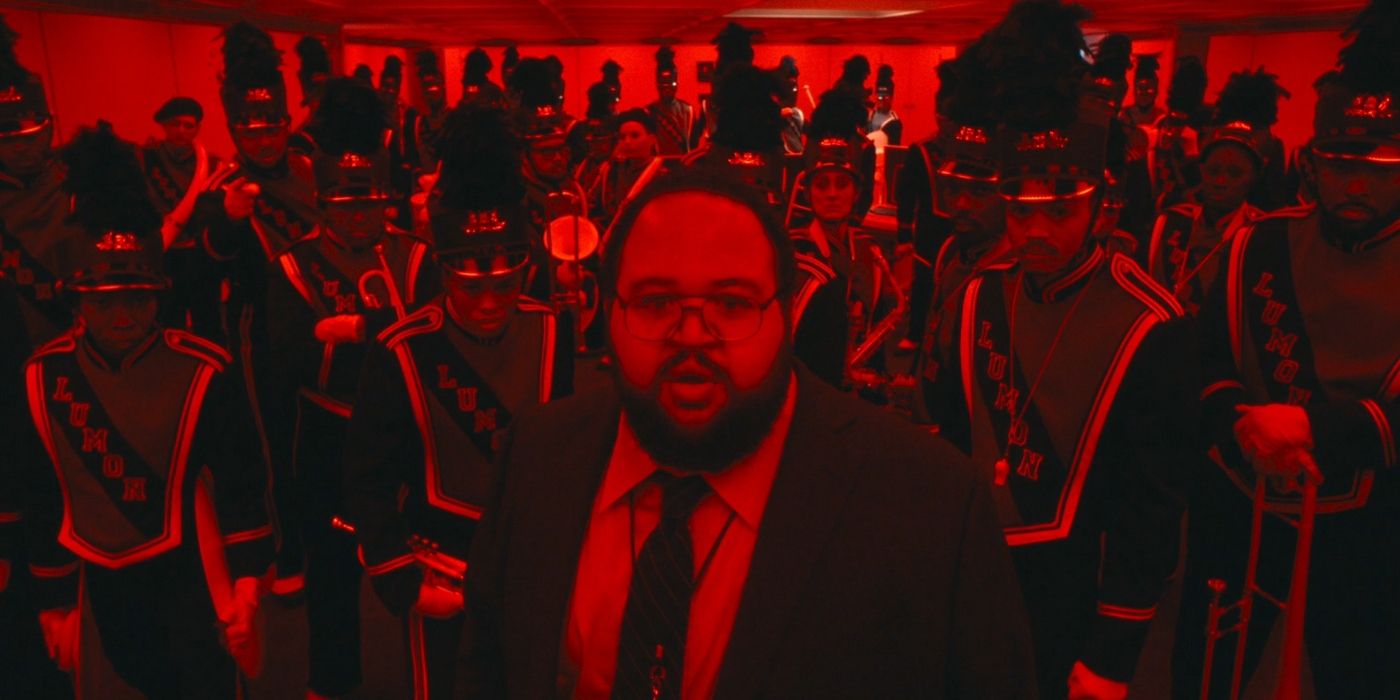 Dylan (Zach Cherry) stands in front of a marching band bathed in red light in Severance Season 2