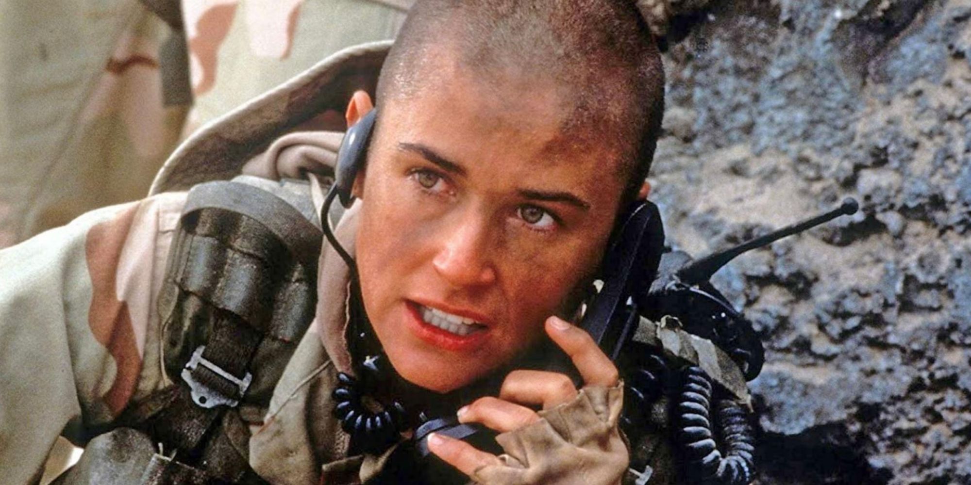 Demi Moore with a shaved head in fatigues speaking into a phone on a battlefield in GI Jane.