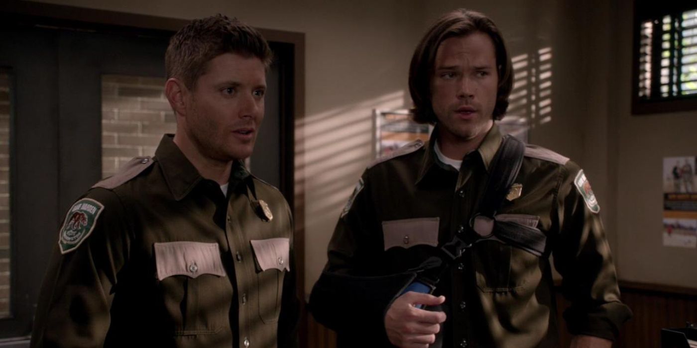 Sam and Dean wear patrol uniforms and stand together in an office in Supernatural.