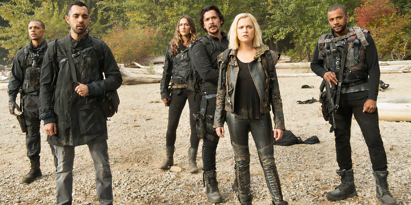 The 100 cast are standing on a beach staring with concern. 